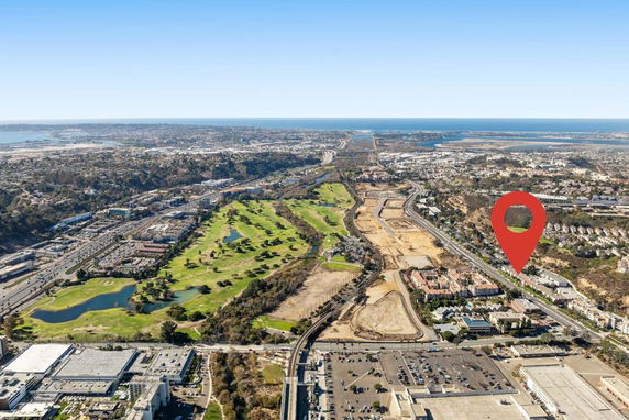 Wide-angle aerial view of an urban landscape with a golf course, roads, commercial and residential areas, and bodies of water in the distance.