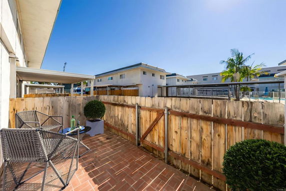 View from a fenced patio area, overlooking neighboring buildings and a pool area.