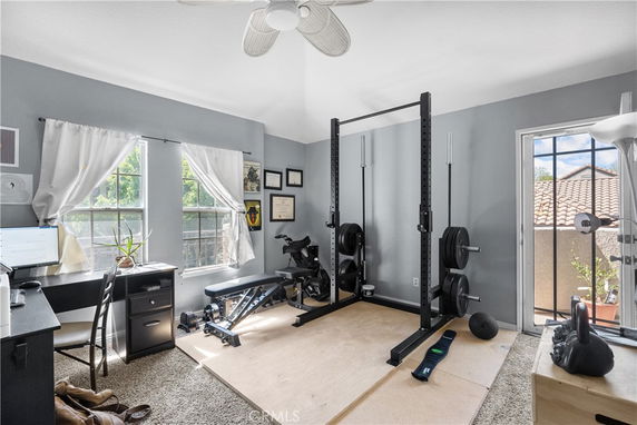 Room with gym equipment including a power rack, bench, and weights.