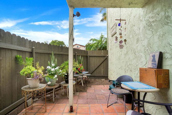 Small outdoor patio with potted plants and chairs against a fenced backyard.