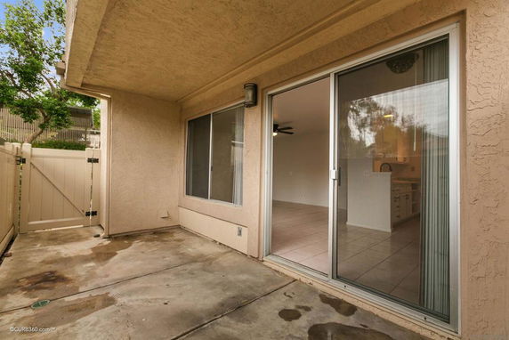 View into a house interior through sliding glass doors from a small fenced outdoor patio.