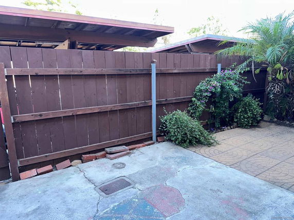 Outdoor covered parking area with adjacent wooden fence and plants