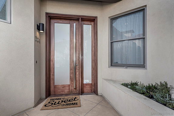 Front view of a house entrance with wooden double doors and a welcome mat.
