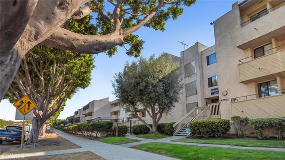Front view of a multi-story apartment building with balconies and a surrounding fence.