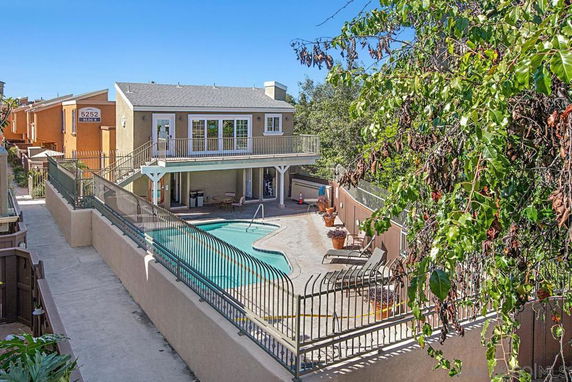 View of a two-story house with a fenced swimming pool area in front.