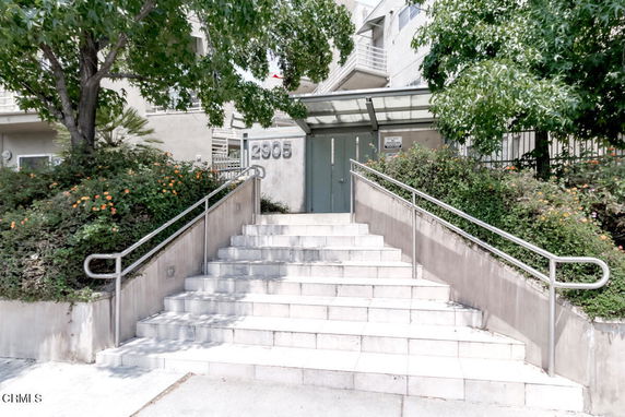 Front view of a building entrance with stairs and a glass canopy.
