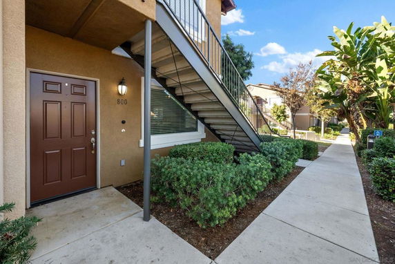 Front view of a building entrance with an exterior staircase and brown door.