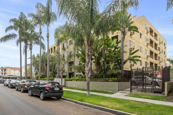 Front view of a multi-story residential building with balconies and an entrance gate.