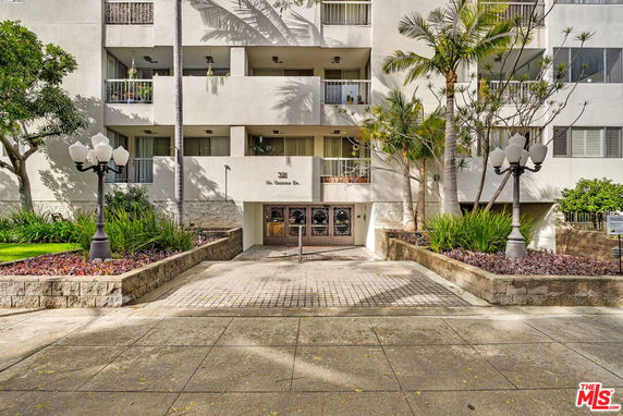 Front view of a multi-story residential building with balconies and landscaped entrance.