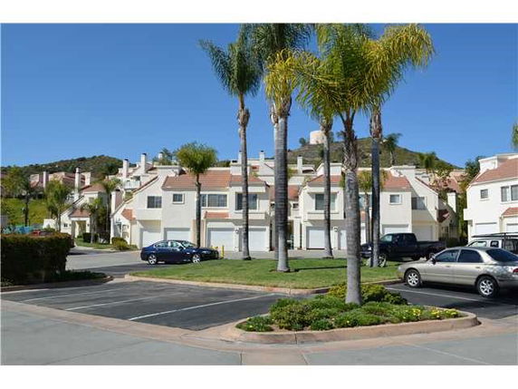 Front view of a row of multi-story townhouses with garages and a parking area.