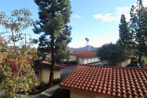 View from a building showing nearby structures with red-tiled roofs and trees.