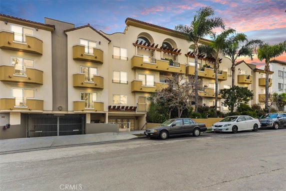 Front view of a multi-story apartment building with balconies and gated parking.