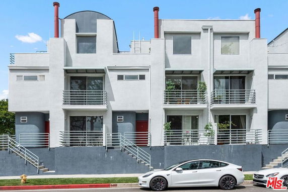 Front view of a modern multi-story building with balconies and red doors.