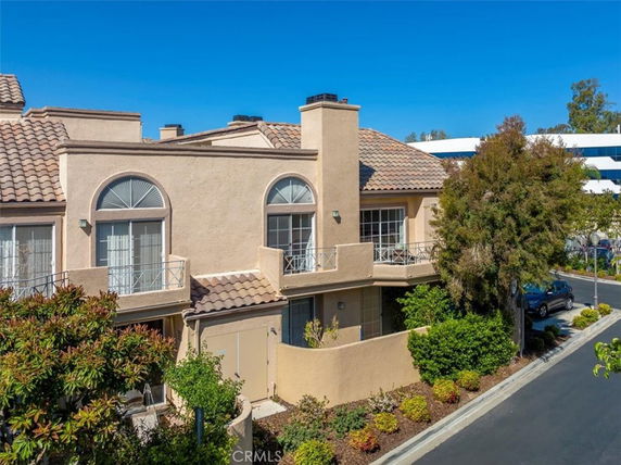 Front view of a multi-story house with beige stucco walls and a tiled roof.