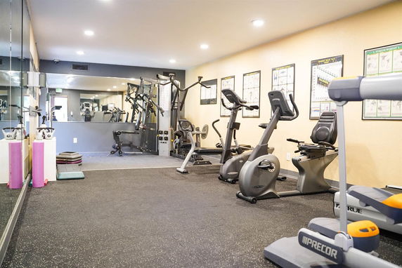 Room with exercise equipment, including stationary bikes and weight machines.