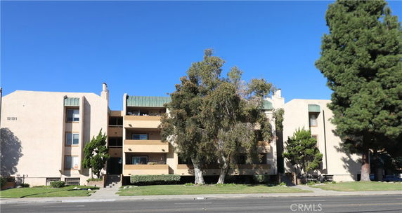 Front view of a multi-story apartment building with balconies and surrounded by trees.