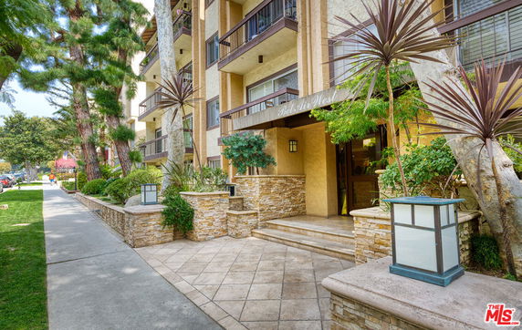Front view of a multi-story building with balconies and a landscaped entrance.