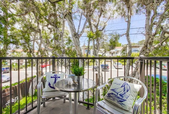 View from a balcony overlooking a street with trees and parked cars.