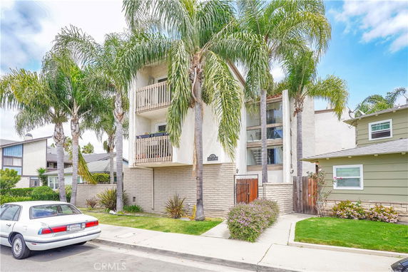 Front view of a three-story building with balconies and palm trees.