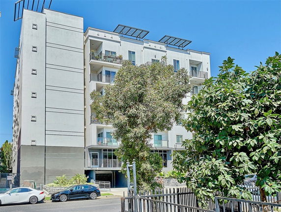 Front view of a multi-story apartment building with balconies and rooftop structures.