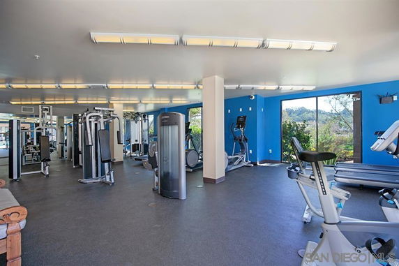 Interior view of a gym with various exercise equipment and large windows.