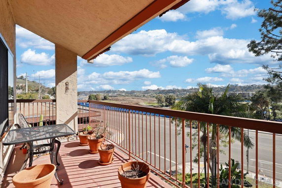 View from a balcony overlooking a road and distant hills with potted plants and a metal table with chairs.