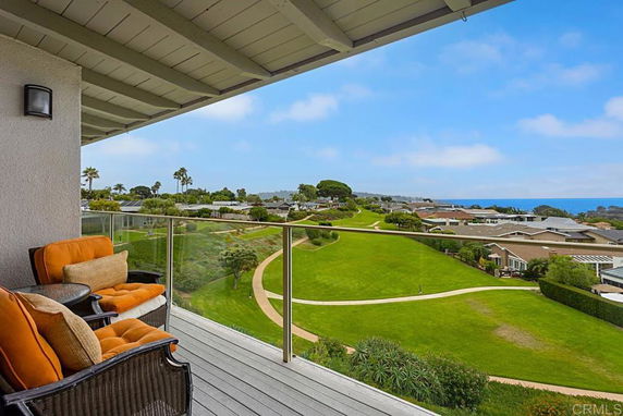 View of a scenic landscape with green lawns and ocean from a balcony.