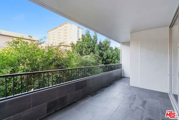Partially covered balcony with railing, overlooking surrounding trees and buildings.