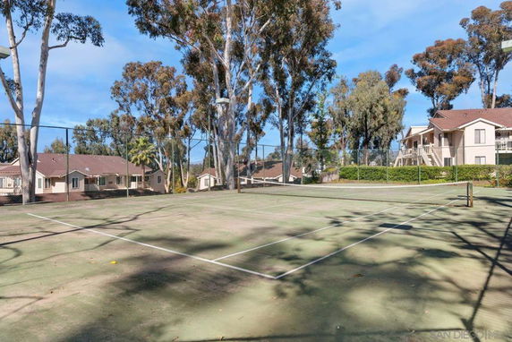 Tennis court surrounded by trees and residential buildings.
