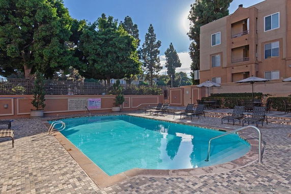 Outdoor swimming pool area with lounge chairs and umbrellas near a building.