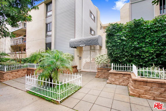 Front view of a multi-story residential building with a gated entrance and small garden.