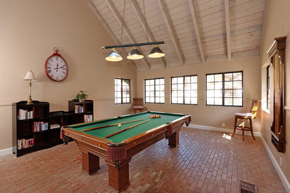 Room with a pool table, bookshelves, a large clock, and slanted wooden ceiling.