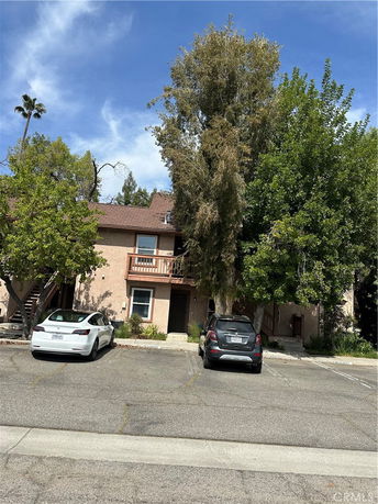 Front view of a two-story house with an open balcony and two parked cars in the driveway.