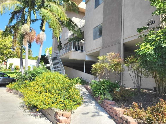 Front view of a multi-story building with external staircase and surrounding greenery.
