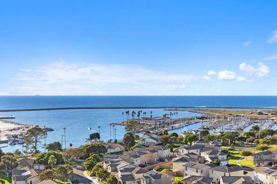Wide-angle view of coastal residential area with a marina and ocean in the background.