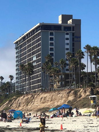 Front view of a multi-story beachfront building with large windows.