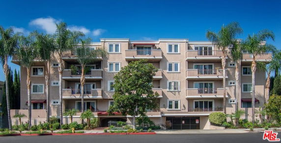 Front view of a multi-story building with balconies and palm trees.