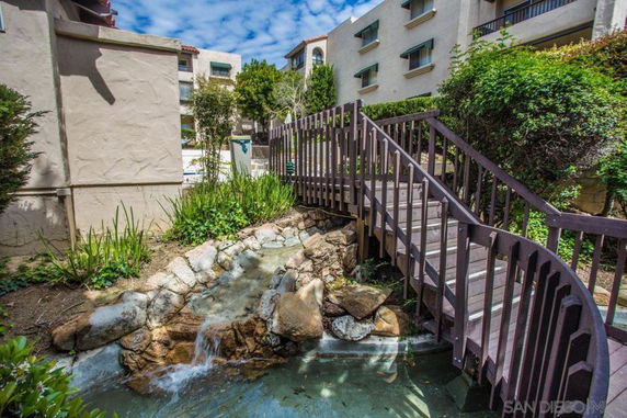 Outdoor view of a building complex with a wooden bridge over a small stream and garden area.