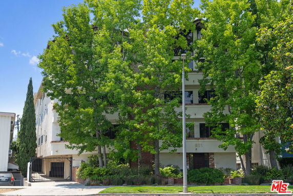 Front view of a multi-story residential building partially obscured by trees.