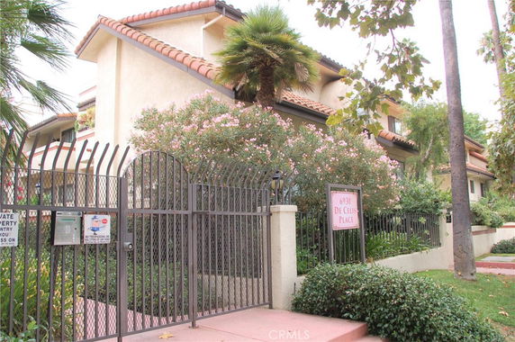 Front view of a multi-story building with a gated entrance and lush greenery.