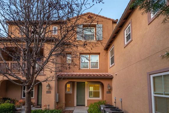 Front view of a multi-story townhouse with stucco exterior and green doors.