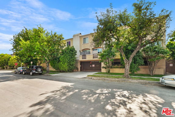 Front view of a multi-story residential building with trees and parked cars on the street.