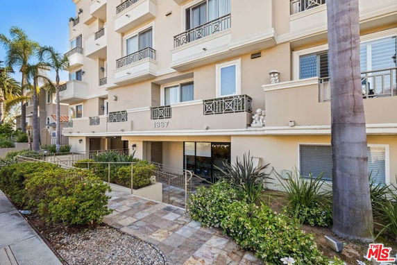 Front view of a multi-story apartment building with balconies and landscaped entrance.