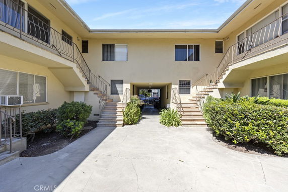Front view of a two-story building with outdoor staircases and shrubbery.