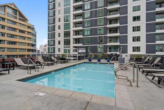 Outdoor swimming pool area with lounge chairs on a high-rise building terrace.