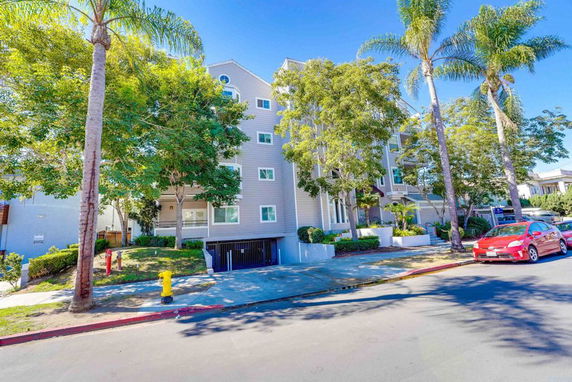 Front view of a multi-story residential building with trees and parking space.