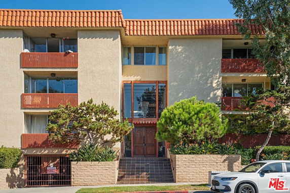 Front view of a multi-story residential building with balconies and a tiled roof.