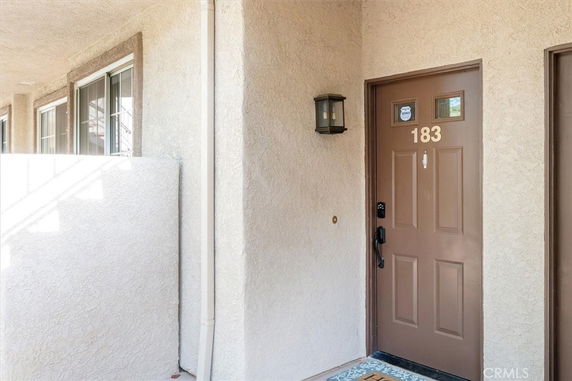 Front view of a building entrance with a brown door numbered 183 and light fixture.