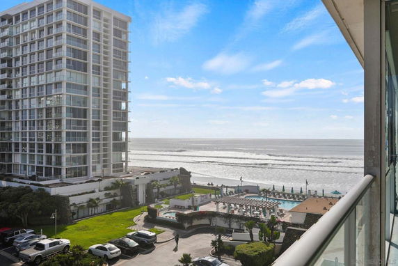 View of a beachfront area with a tall residential building and a swimming pool near the ocean.