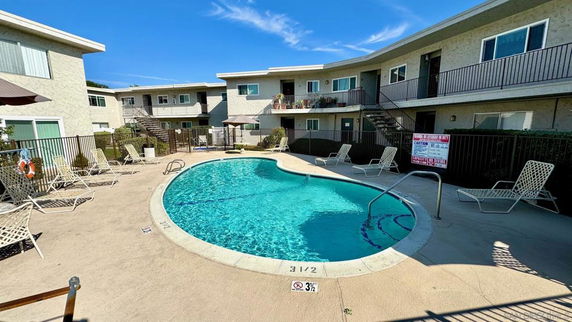 Outdoor swimming pool area surrounded by a two-story residential building.